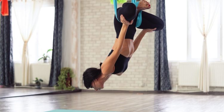 Adult woman practices anti-gravity yoga position in studio