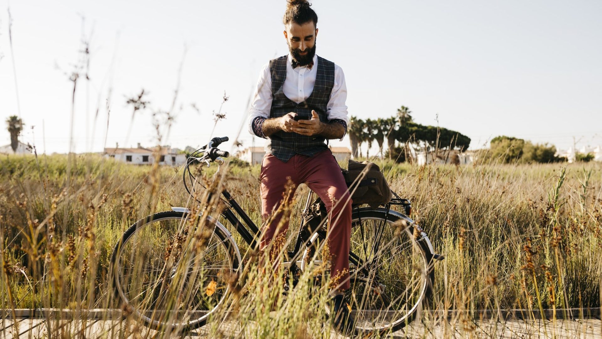 Well dressed man with his bike on a wooden walkway in the countryside using cell phone